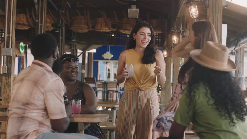 A group of people are laughing and talking with drinks outdoor at a restaurant