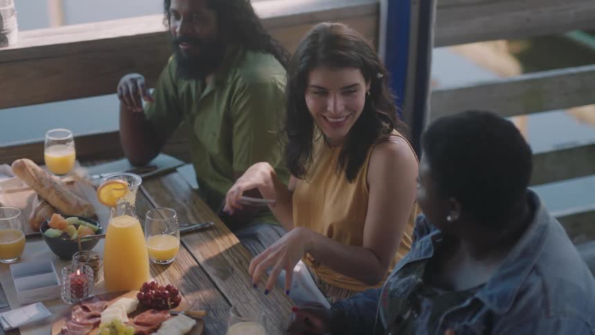 Friends laugh and chat over drinks and food while sitting outisde