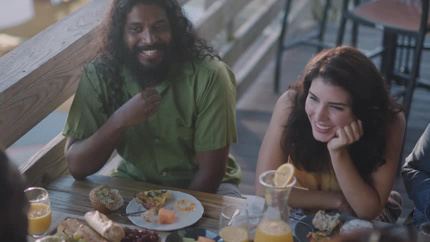 Friends talk and laugh sitting at outdoor table near wooden rail