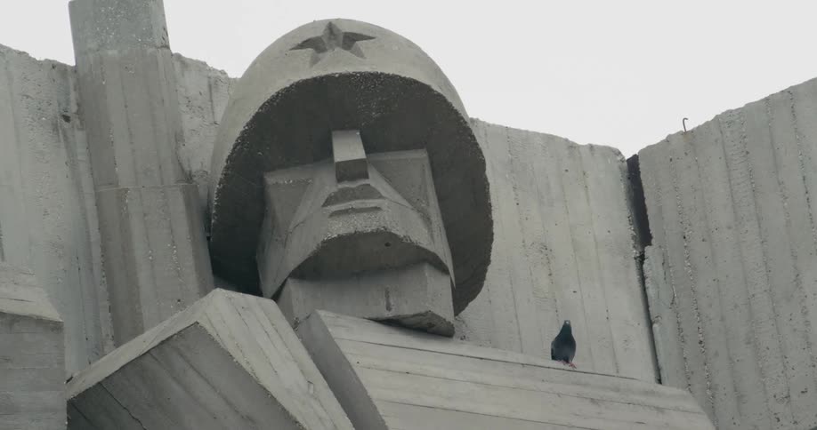 A bird sitting on a monument of soldier head with a star on the helmet flies away