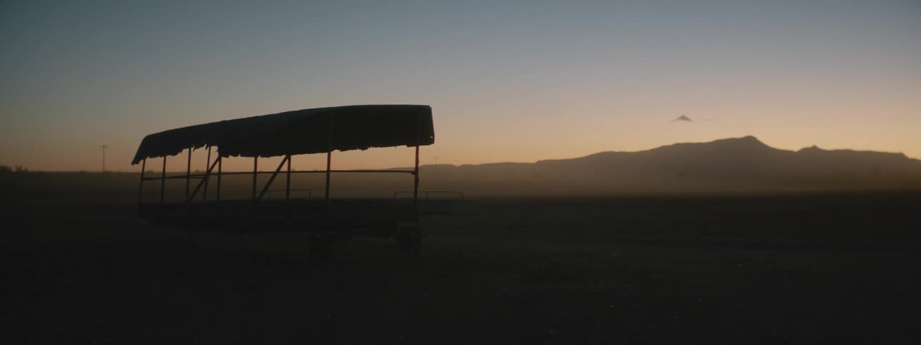 A tarp covered shelter is on open land with mountains in the distance