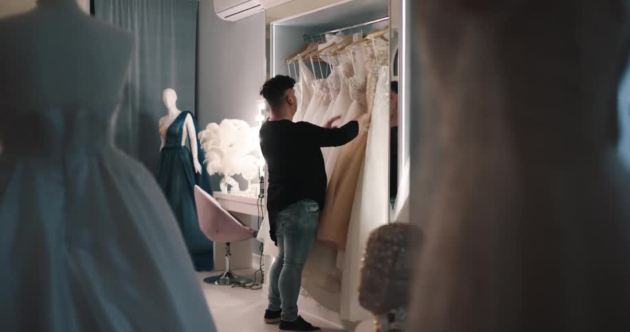 A fashion designer removes a wedding dress from a closet and carries it away
