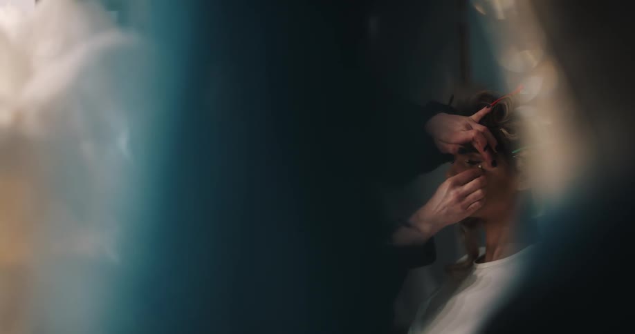 A woman sitting in a room as another woman applies makeup to her face