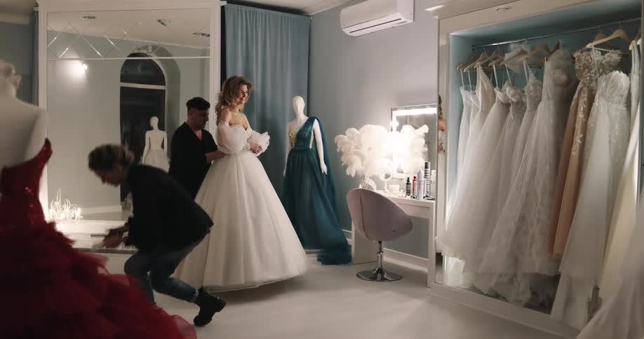 Bridal shop workers help bride try on wedding dress
