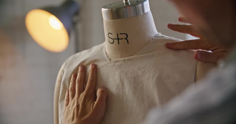 A person uses pins to secure clothes over a mannequin