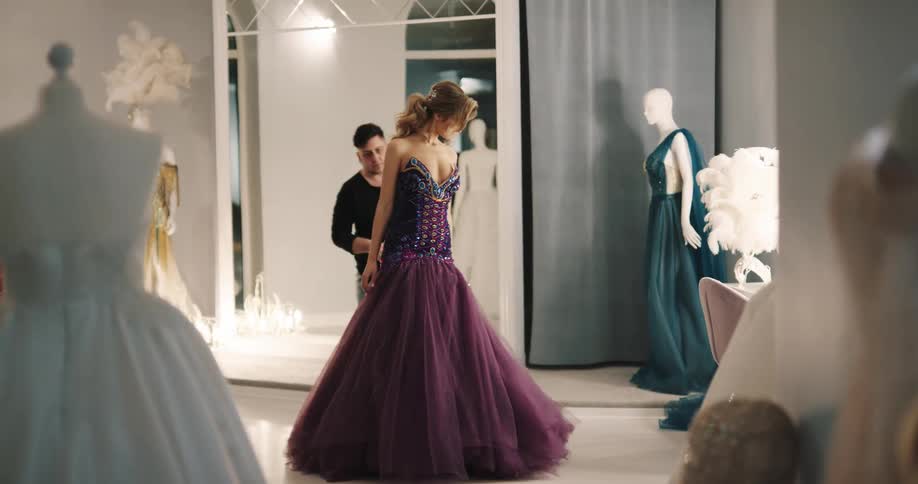 A man trims a womans dress skirt before the woman begins to test the movement of the skirt