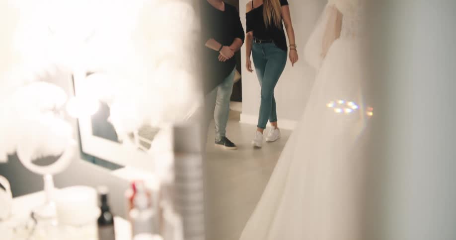 A woman is wearing a wedding gown and two people are helping her get ready