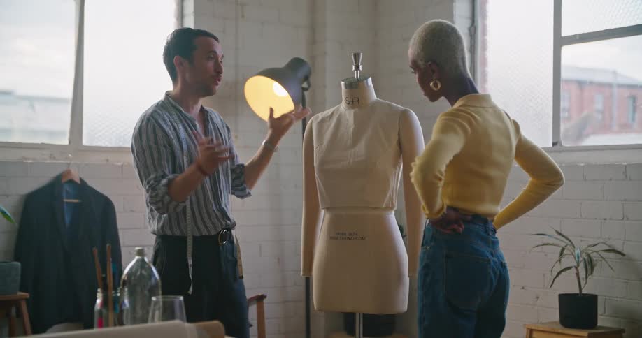 Two designers stand next to a dress form discussing a design