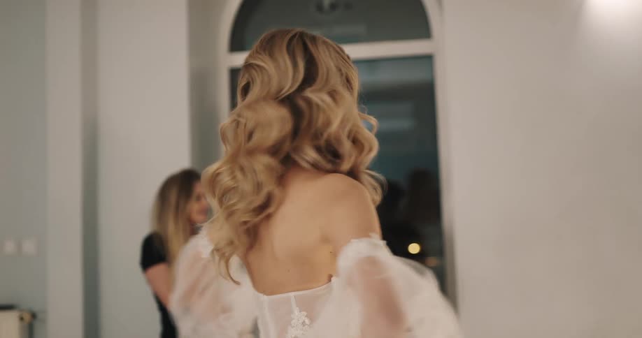 A woman admires a designer wedding gown she is wearing then turns and hugs the stylist and designers