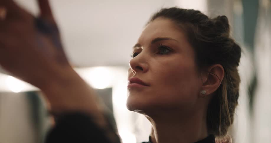 A makeup artist does a womans makeup in a dressing room