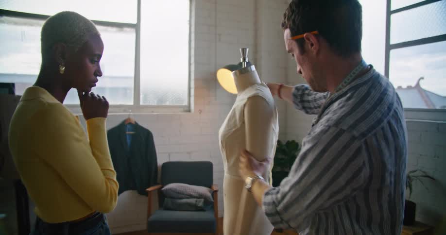 A man and woman designing clothing look at a shirt on a mannequin