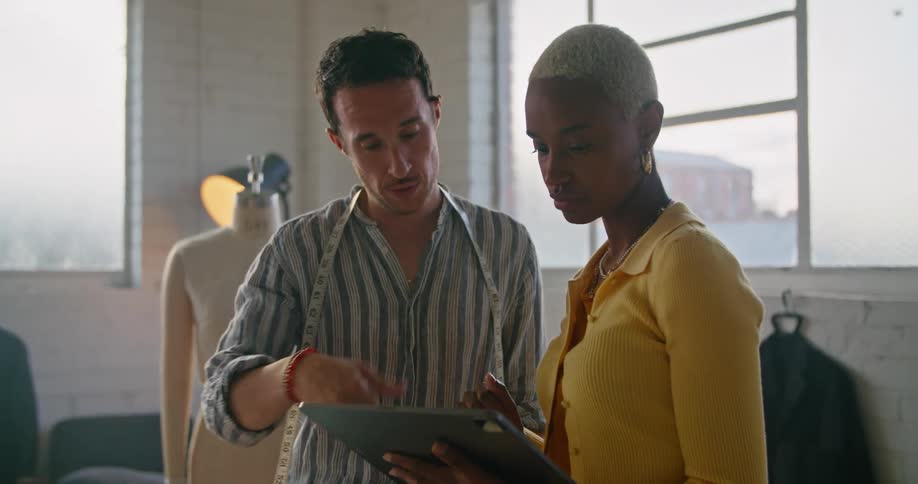Clothing designers are having a discussion using a tablet in a design studio during the day