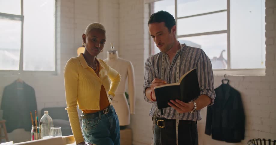 A man in an office shows a woman information in a book and they talk