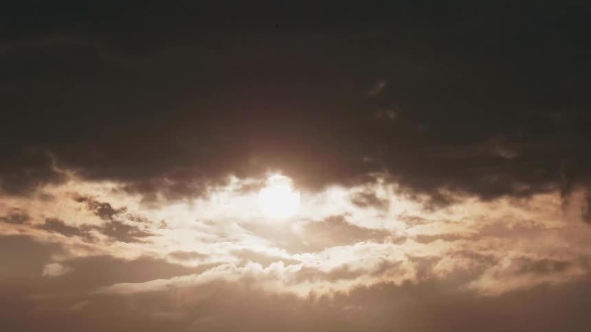 Sun rises in sky becoming obscured by dark clouds
