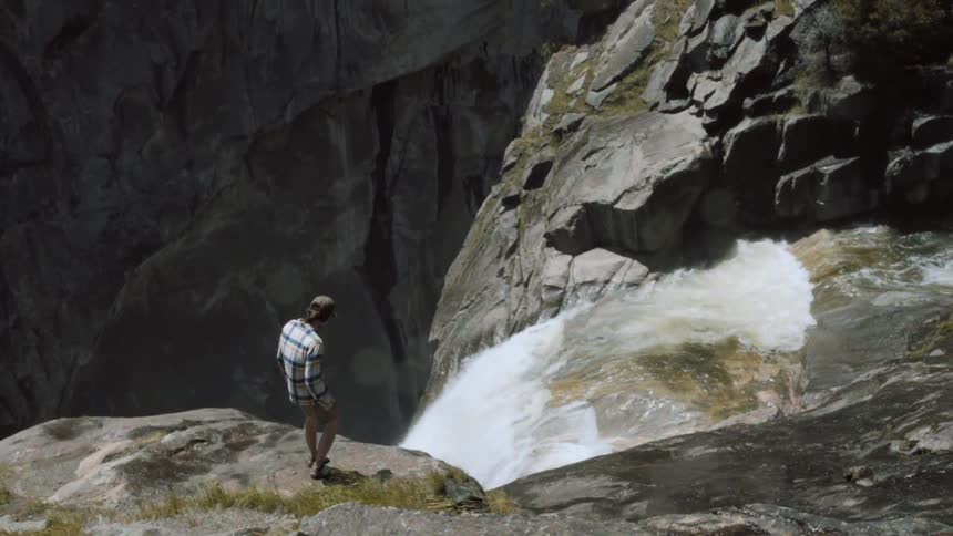 A man walks near the edge of a waterfall below