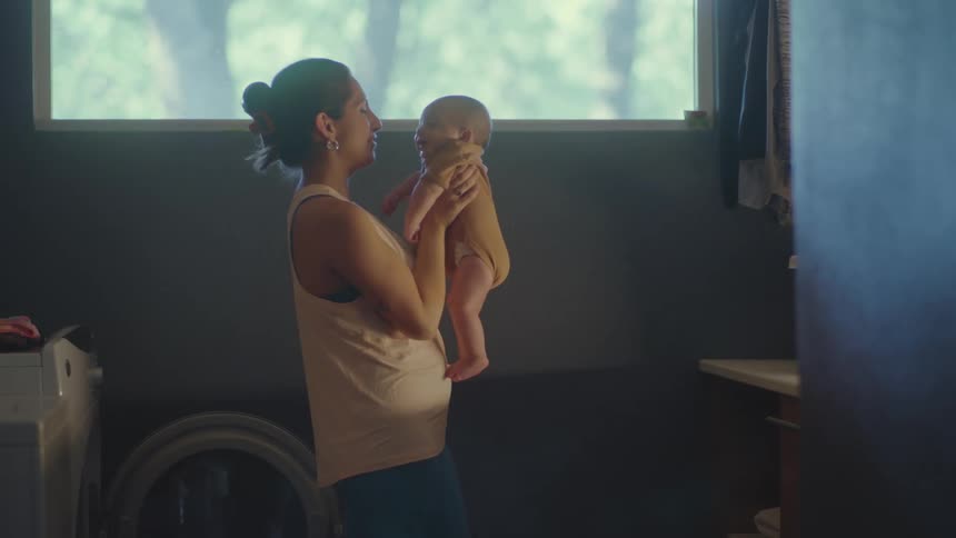 A woman playfully rubs her nose against the nose of an infant she is holding