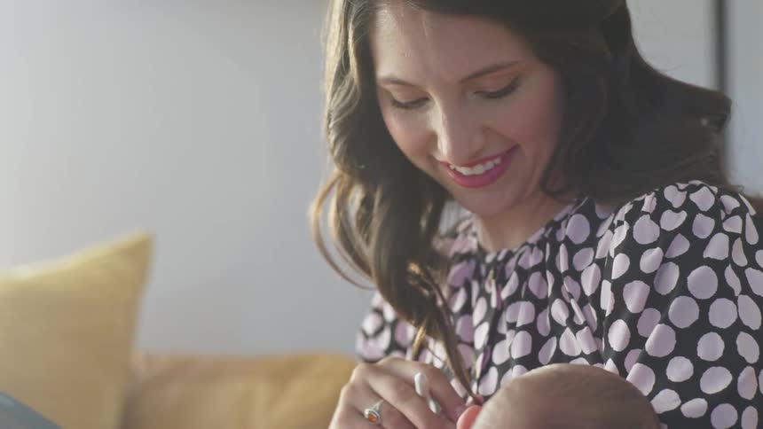 A woman in a room sitting on a couch holding a baby a stylus and a tablet