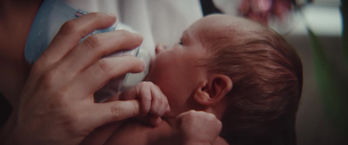 Baby holds pinky finger of person holding and feeding them from bottle
