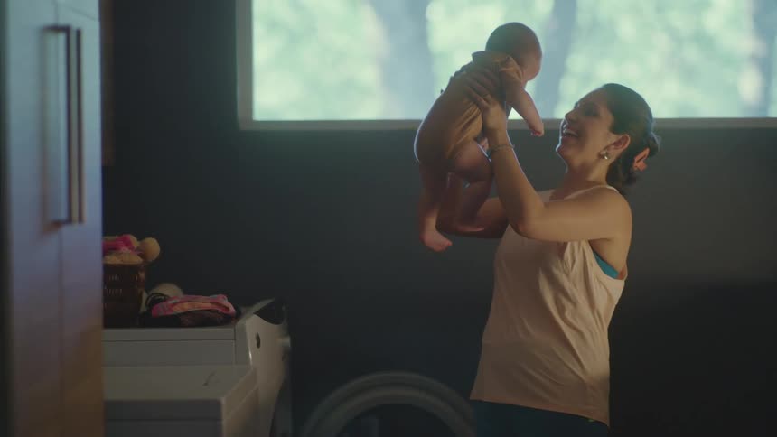 A woman holds her baby up in a laundry room and smiles