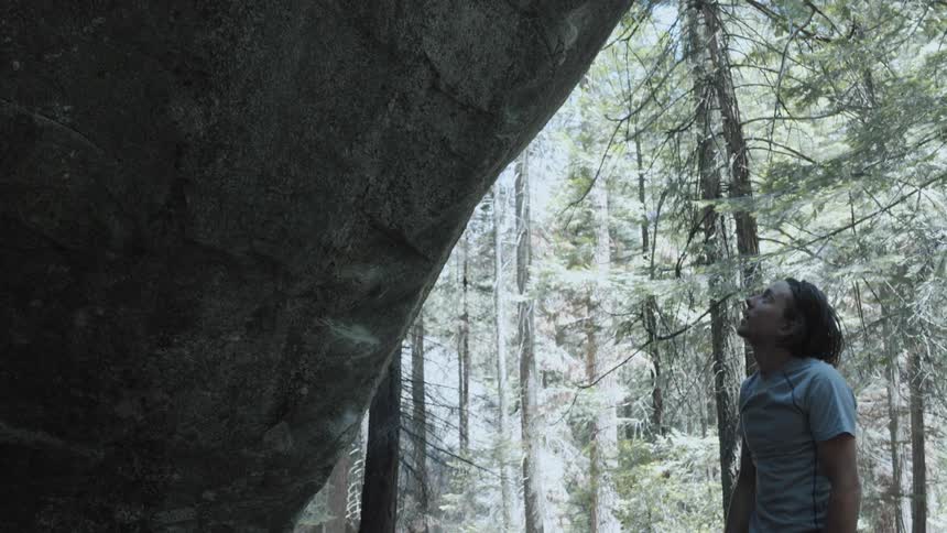 A man looks up at a rock wall in front of him