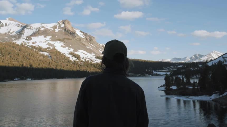 A man stands before a lake with a mountain in the distance
