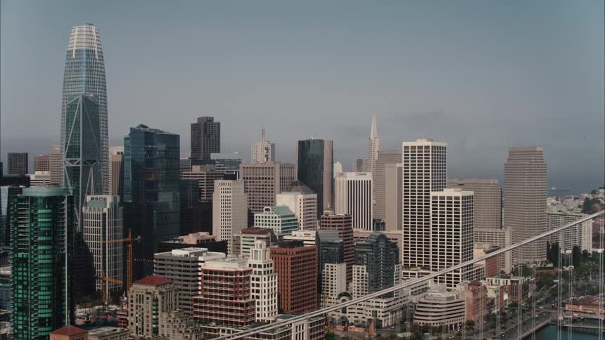 A city skyline with buildings and skyscrapers with a bridge in the foreground and the sky and clouds in the background