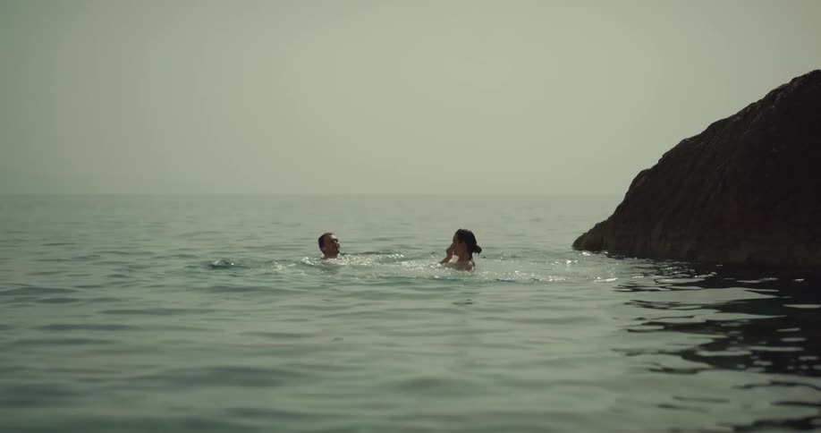 Woman in bikini jumps off low cliff and kisses man in sea