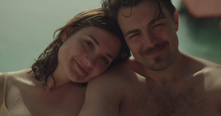 A woman rests her head on her boyfriends shoulder as they relax in a pool and kiss