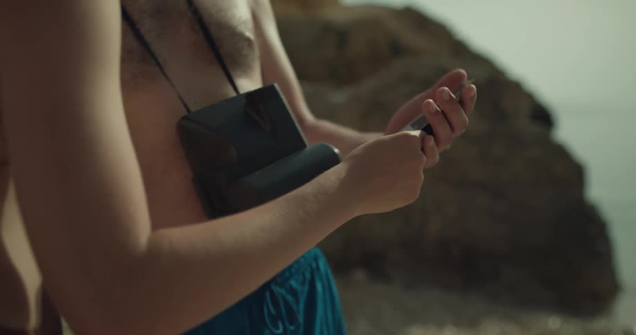 A man and a woman are on a beach wearing swimming clothes and looking at pictures they are taking with a polaroid camera