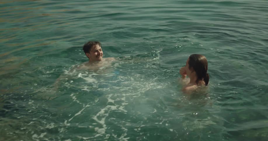 A man and woman laugh and play in the water as they do somersaults and splash one another