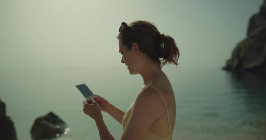 A man takes a polaroid picture of his girlfriend on the beach