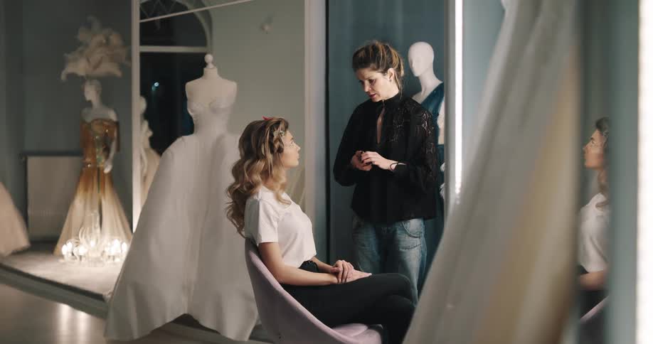 A woman sits in a chair as another woman explains a fitting to her