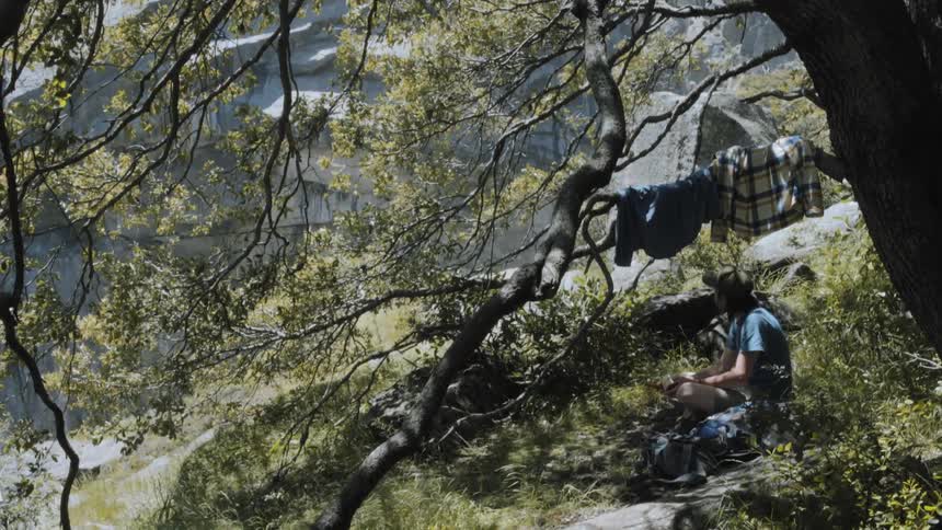 A man sits below his hanging clothes on a hill