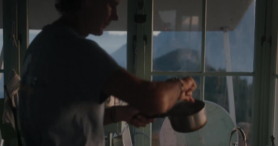 A man stirs something in a pot inside a small kitchen area