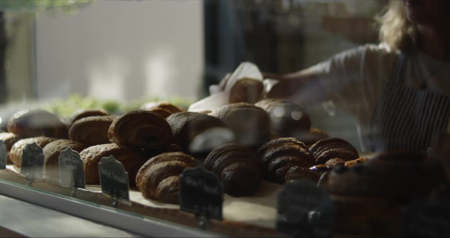 Woman takes croissant from pastry display case in the bakery