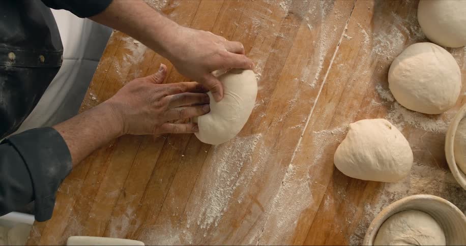 A man picks up a ball of dough and begins to knead it as he bakes bread