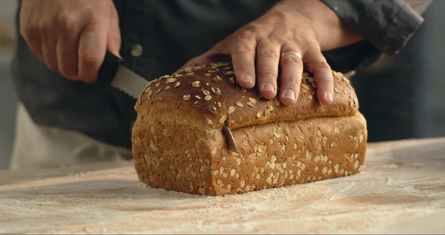 Man slices bread on wooden surface coated with flour