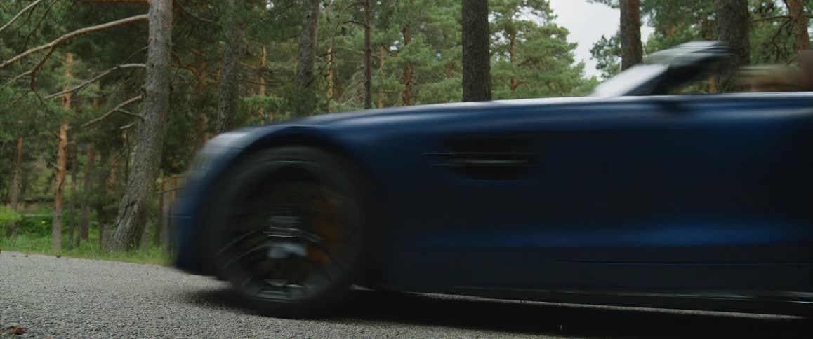 Blue sports car driving on a gravel road next to the forest