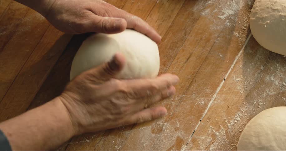 Man kneading bread dough over a wooden table