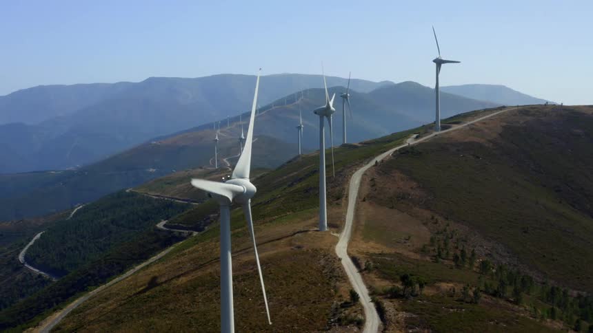 Wind turbines spinning on a wind farm with mountains in the distance