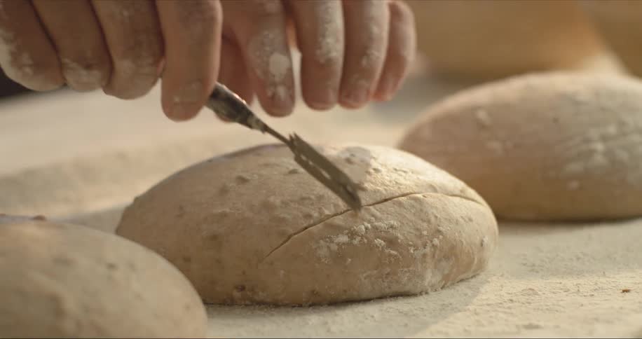 A baker is scoring bread dough with a knife