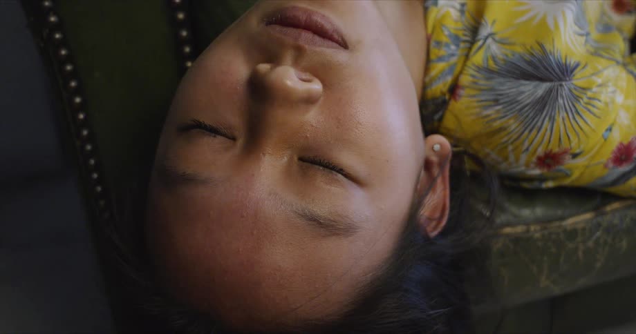A girl sleeping on a leather couch with her head hanging over the side opens her eyes