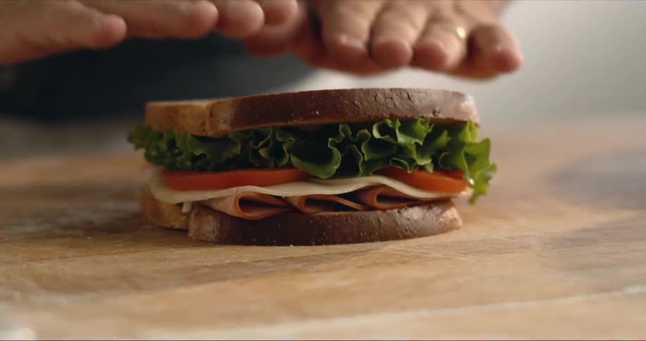 A person in a room making a sandwich on a table with a wall in the background
