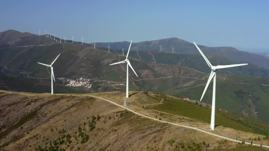 Wind turbines spinning on a wind farm with mountains in the distance