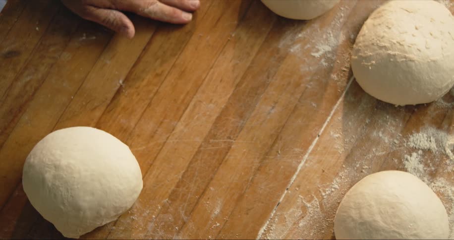 Man kneads dough on wooden surface he dusts with flour
