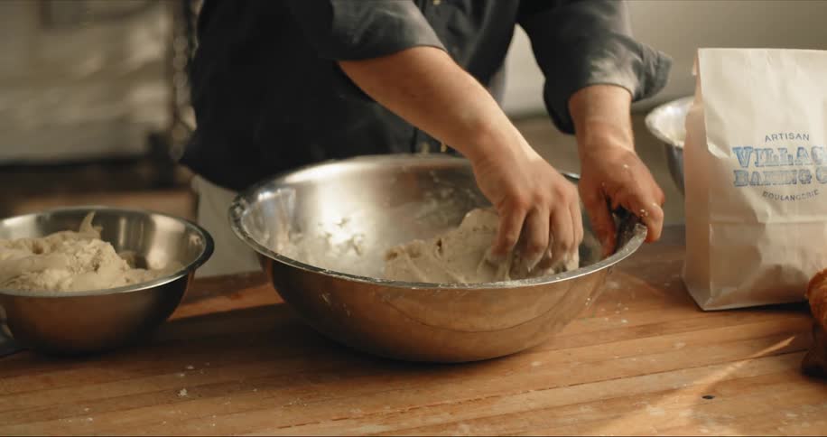 Chef kneading bread dough on a metallic bowl over a table