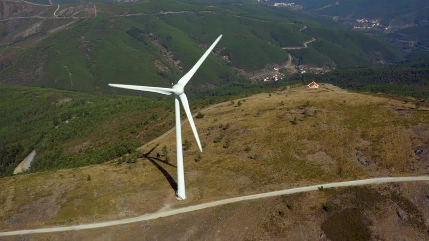 Aerial view of a wind turbine spinning on the top of a mountain