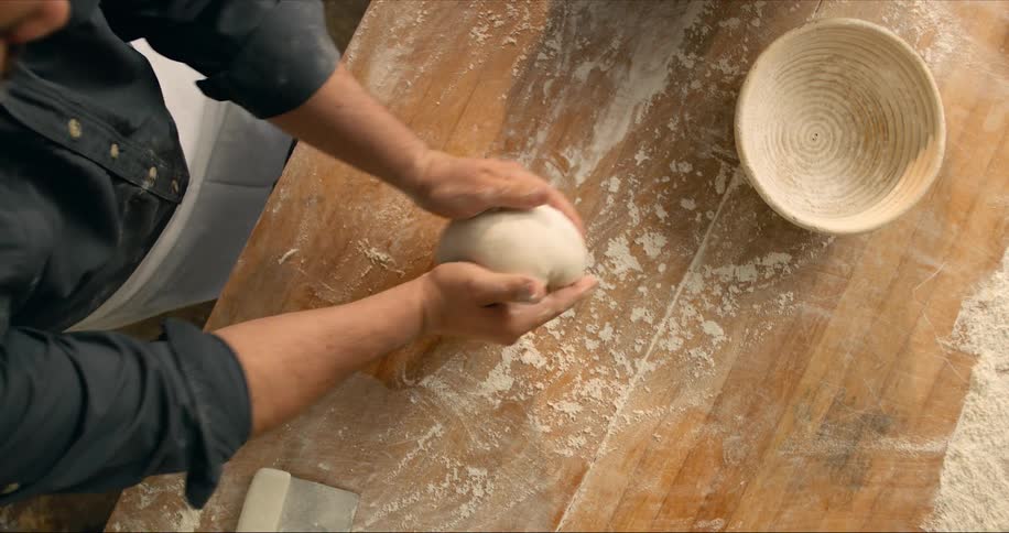 A man kneading dough on a table with flour and a basket