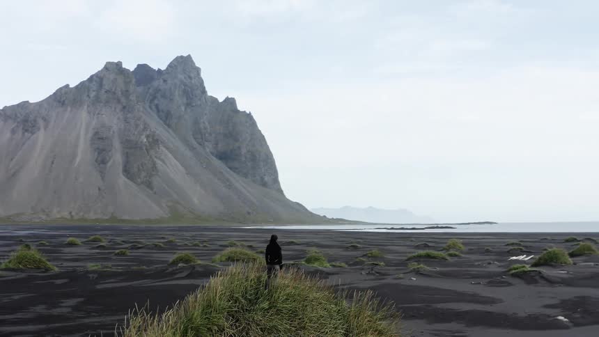A person in a landscape near the coast with a mountain range the sky and clouds in the background