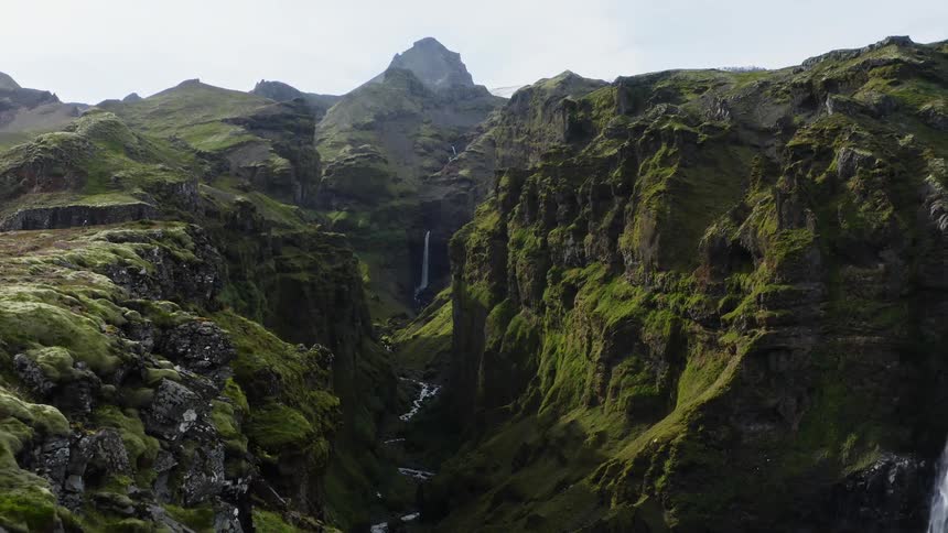 A person sits on the edge of a cliff across from a water fall as bird fly in the valley